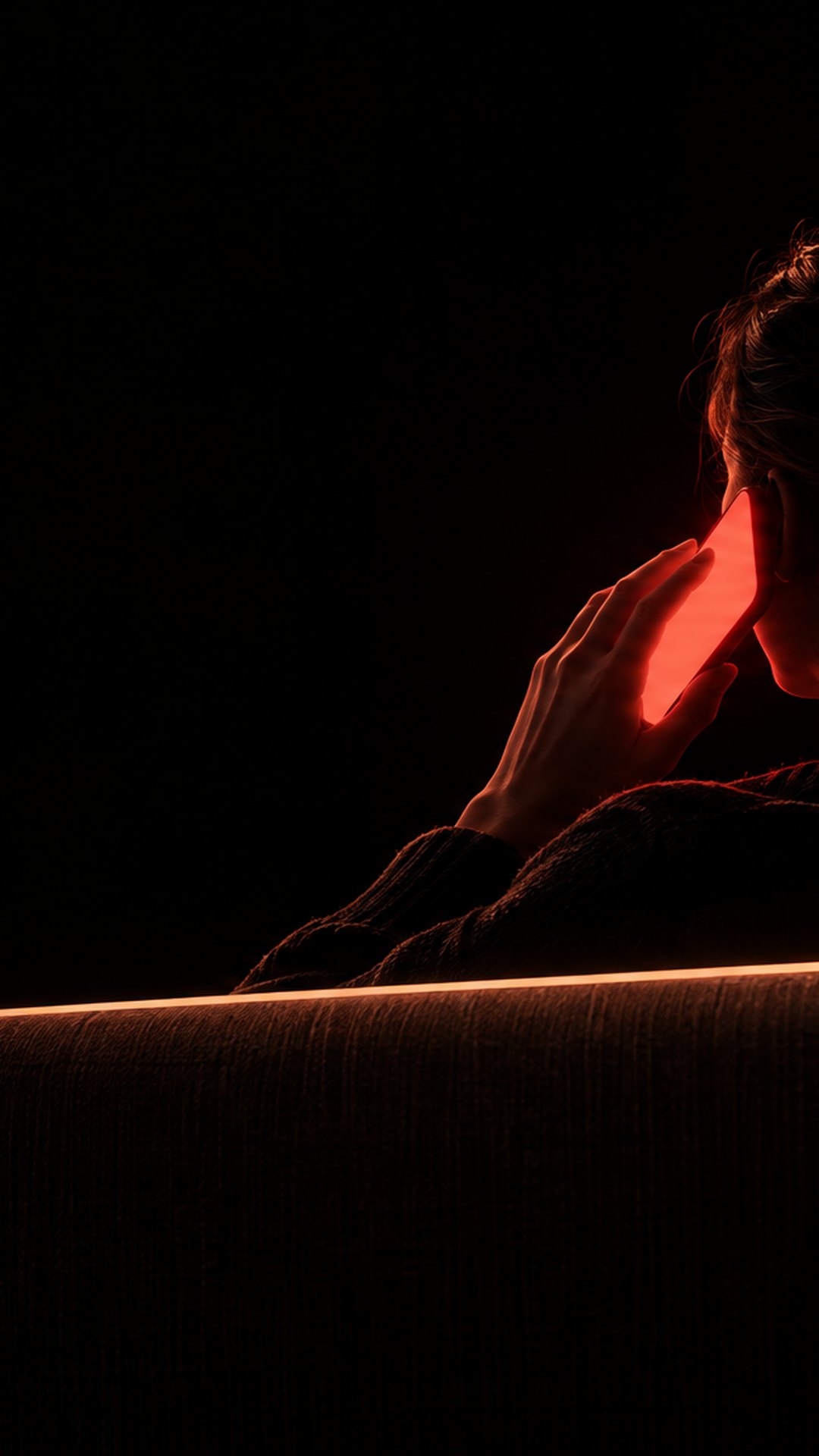 A person on a sofa at night taking a call, the phone screen lighting their hand
